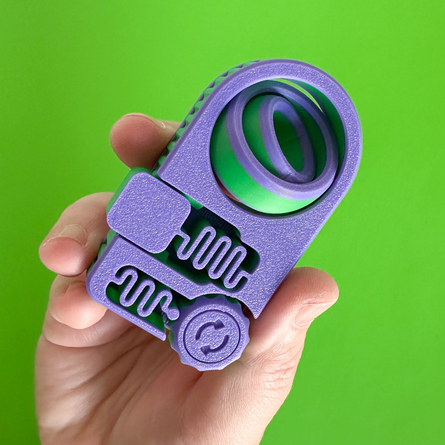 A purple and green panel shaped fidget toy with a click wheel, a push button and a gyro spinner held by a hand