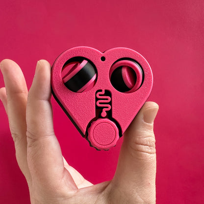 A pink and black heart shaped fidget toy with two gyro spinners and a click wheel