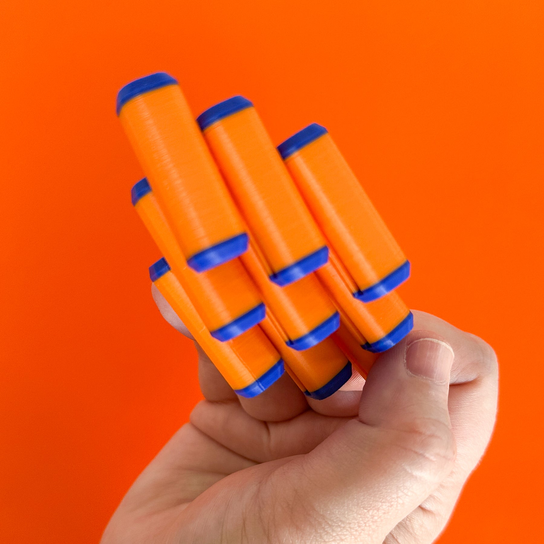 A blue and orange cube shaped fidget spinner splayed out to show its moving parts and rods held by a hand on an orange backdrop