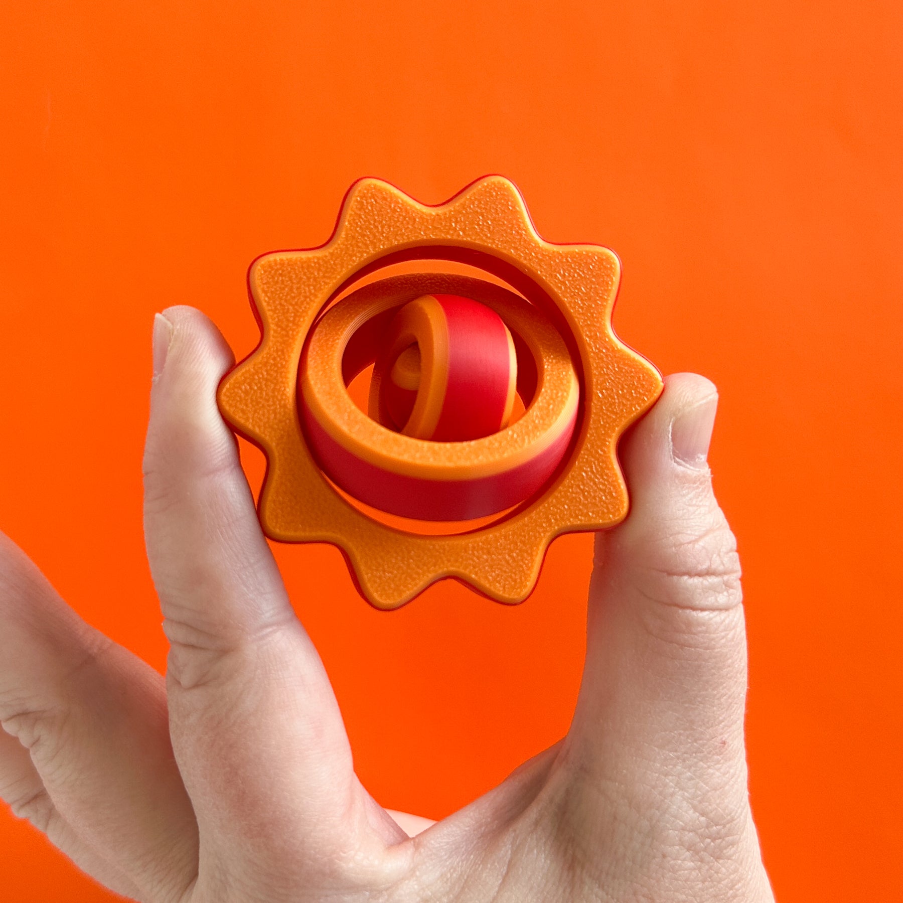 An orange and red fidget spinner with a sine wave outer shape
