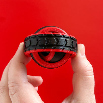 A red and black fidget spinner with texture like a tire held by a hand
