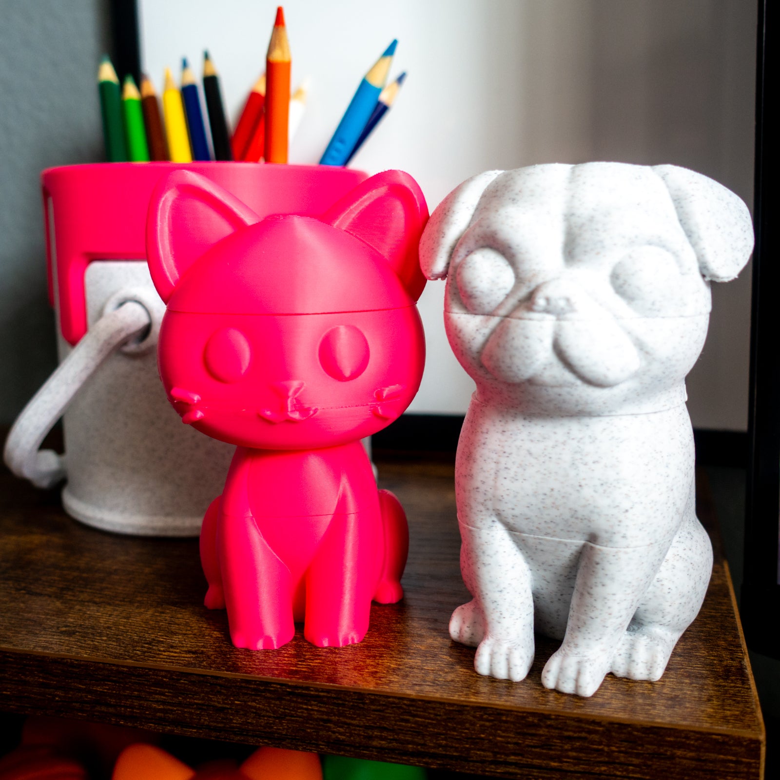 Whisk the cat and Wrinkle the pug paired beside a paint can, illustrating desk-friendly size and collectible appeal